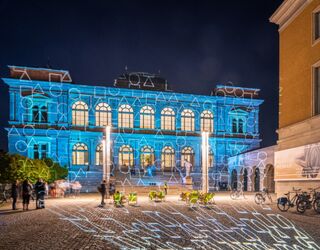 Museum Neues Das Museum Weimar wird von blauen Lichtern beleuchtet, während Passanten und Fahrräder die lebendige Atmosphäre genießen.