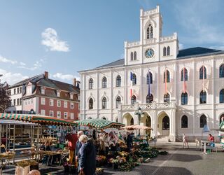 Rathaus auf dem Marktplatz Ein belebter Marktplatz mit bunten Ständen, umgeben von historischen Gebäuden und einer strahlend blauen Himmel.