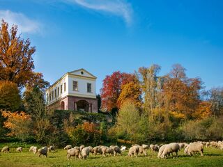 Römisches Haus, Foto: Matthias Eckert Eine malerische Landschaft mit einem römisch anmutenden historischen Gebäude, umgeben von bunten Herbstbäumen und einer Herde von Schafen.