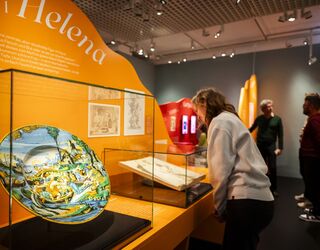 Ausstellungsimpression Faust. Eine Ausstellung Eine Person betrachtet fasziniert eine kunstvolle, bemalte Schale im Schiller-Museum, umgeben von weiteren Ausstellungsstücken.