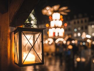 Weimarer Weihnacht bei Nacht Eine beleuchtete Laterne hängt an einem Holzpfosten, während im Hintergrund festliche Lichter und Stände zu sehen sind.