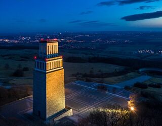 Nachtansicht Glockenturm Gedenkstätte Buchenwald, Foto: Peter Hansen Im Vordergrund ist ein imposanter Turm zu sehen, der von warmem Licht erhellt wird, während der Himmel in sanften Blautönen leuchtet.