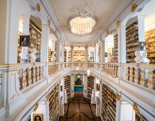 Anna Amalia Bibliothek Der Blick auf eine opulente Bibliothek mit goldenen Verzierungen, hohen Decken und einer zentralen Treppe, die zu weiteren Regalen führt.