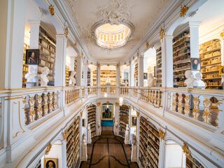 Anna Amalia Bibliothek Der Blick auf eine opulente Bibliothek mit goldenen Verzierungen, hohen Decken und einer zentralen Treppe, die zu weiteren Regalen führt.
