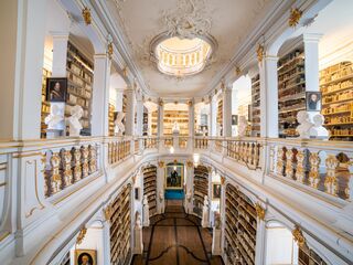 Rokokosaal Herzogin Anna Amalia Bibliothek, Foto: Alexander Burzik, weimar GmbH Der Blick auf eine opulente Bibliothek mit goldenen Verzierungen, hohen Decken und einer zentralen Treppe, die zu weiteren Regalen führt.