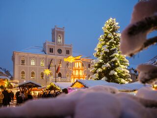 Weimarer Weihnacht Markt Ein festlich geschmückter Weihnachtsmarkt mit einem beleuchteten Weihnachtsbaum und schneebedeckten Ständen in der Dämmerung.