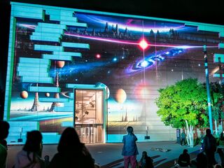 Genius Loci Die Fassade eines Gebäudes ist mit einer bunten Projektion von Planeten und Sternen während Genius Loci geschmückt, während Menschen davor stehen.