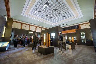 Besucher an Hörstation in der Ausstellung, Foto: Thomas Müller, Museum Zwangsarbeit im Nationalsozialismus Ein eleganter Raum mit hohen Decken beherbergt eine Kunstinstallation, während Menschen die Exponate betrachten und diskutieren.