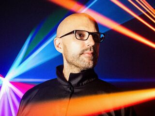 Ein Mann im Fokus mit bunten Lichtstrahlen im Hintergrund Ein Mann mit Glatze und Brille steht vor einem bunten Lichtspiel aus roten, blauen und grünen Strahlen.