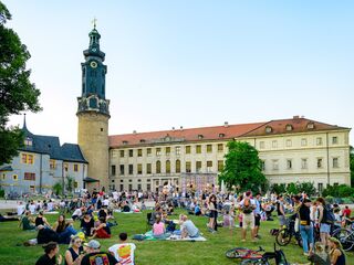 Stadtschloss Familien und Freunde genießen einen sonnigen Tag im Freien, während der alte Uhrturm und die Architektur im Hintergrund sichtbar sind.