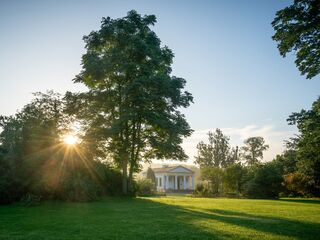 Roemisches Haus im Park an der Ilm Die sanften Strahlen der Morgensonne durchdringen das Laub, während ein historisches Gebäude in der Ferne sichtbar ist.