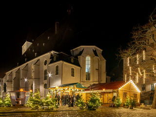 Weimarer Weihnacht Stadtkirche St. Peter und Paul Ein festlich beleuchteter Weihnachtsmarkt mit geschmückten Tannenbäumen und einem einladenden Holzstand in der Nacht.