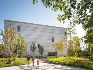 Bauhaus-Museum Weimar, Foto: Thomas Müller, weimar GmbH Ein modernes, helles Gebäude steht im Vordergrund, während zwei Menschen in lässiger Kleidung auf einem Weg vorbeigehen.