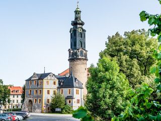 Bastille und Stadtschloss Weimar, Foto: Clemens Bauerfeind, weimar GmbH Die Architektur eines alten Gebäudes mit einem beeindruckenden Turm, umgeben von Bäumen und einem Parkplatz im Vordergrund.