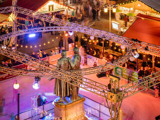 Weihnacht Ein lebendiger Weihnachtsmarkt mit einer Statue im Zentrum, umgeben von festlich dekorierten Ständen und fröhlichen Besuchern.