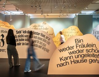 Ausstellungsimpression Faust. Eine Ausstellung Eine Person steht vor einer Wand mit großen, künstlerischen Texten, die emotionale und nachdenkliche Themen ansprechen.