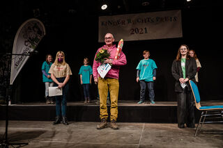 Dirk Wendelmuth auf der Bühne mit der Kinderjury im Hintergrund. 