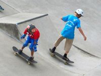 Jugendliche fahren auf Skateboards eine Skateboard-Rampe herab.
